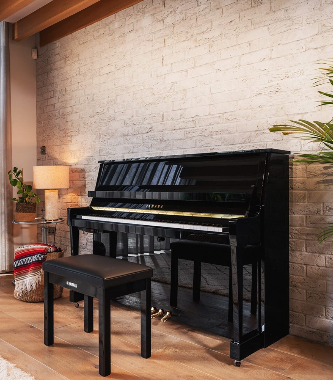 Yamaha B-serie akoestische piano in zwart hoogglans, sfeervol geplaatst tegen een bakstenen muur, als voorbeeld bij de uitleg over de Yamaha B10