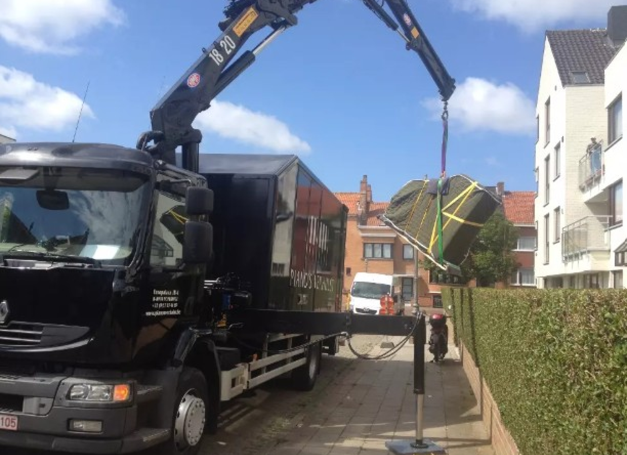 Vrachtwagen van Piano's Verhulst hijst een vleugel met een kraan naar boven tijdens een verhuizing in stedelijke omgeving